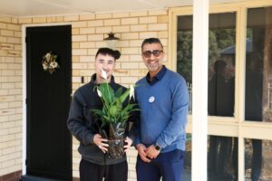 2 men standing in front of front door, holding flowers